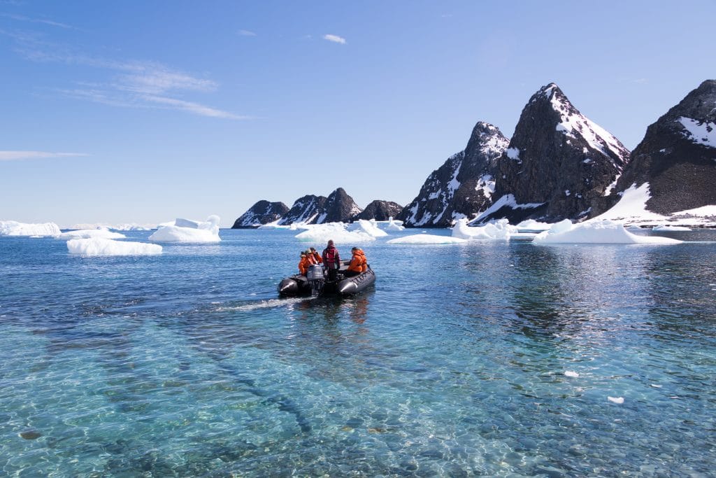 A zodiac floating through a turquoise bay with icebergs and mountains. #antarctica