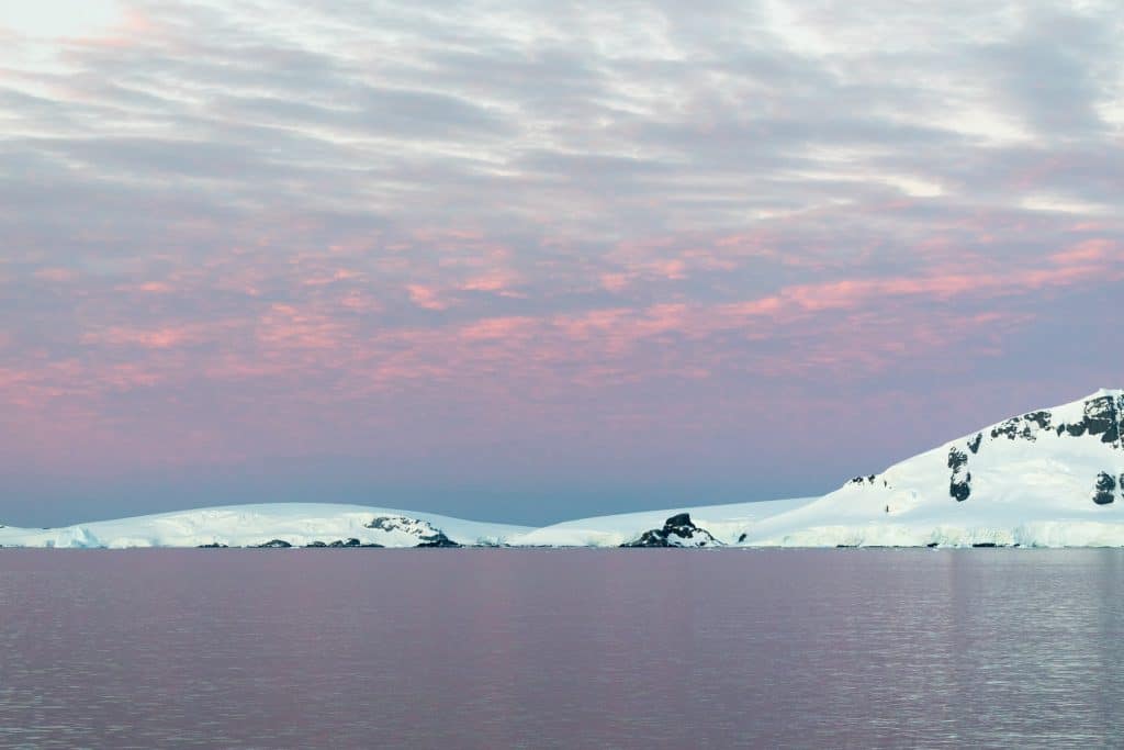 A pink sunset and white snowy hills reflected in the ocean in Antarctica. #antarctica