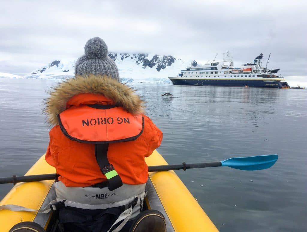 A girls kayaking near a ship in Antarctica. Discover the many reasons to visit Antarctica, and what to expect when you get there. From impressive icebergs to playful penguins and more! #antarctica