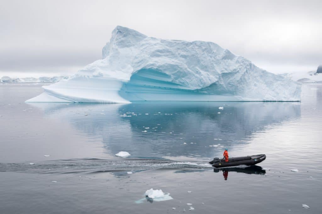 A zodiac floating in front of an iceberg. Discover the many reasons to visit Antarctica, and what to expect when you get there. From impressive icebergs to playful penguins and more! #antarctica