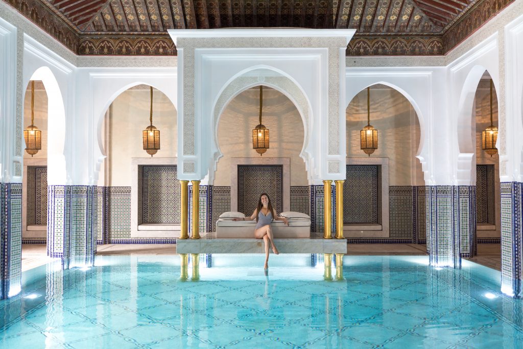 A girl sitting on the edge of a pool with Moroccan decor. Discover the many alluring reasons to visit Marrakesh, Morocco. From must-see sights to can't-miss experiences, here's the very best of Marrakesh! #marrakesh #lamamounia