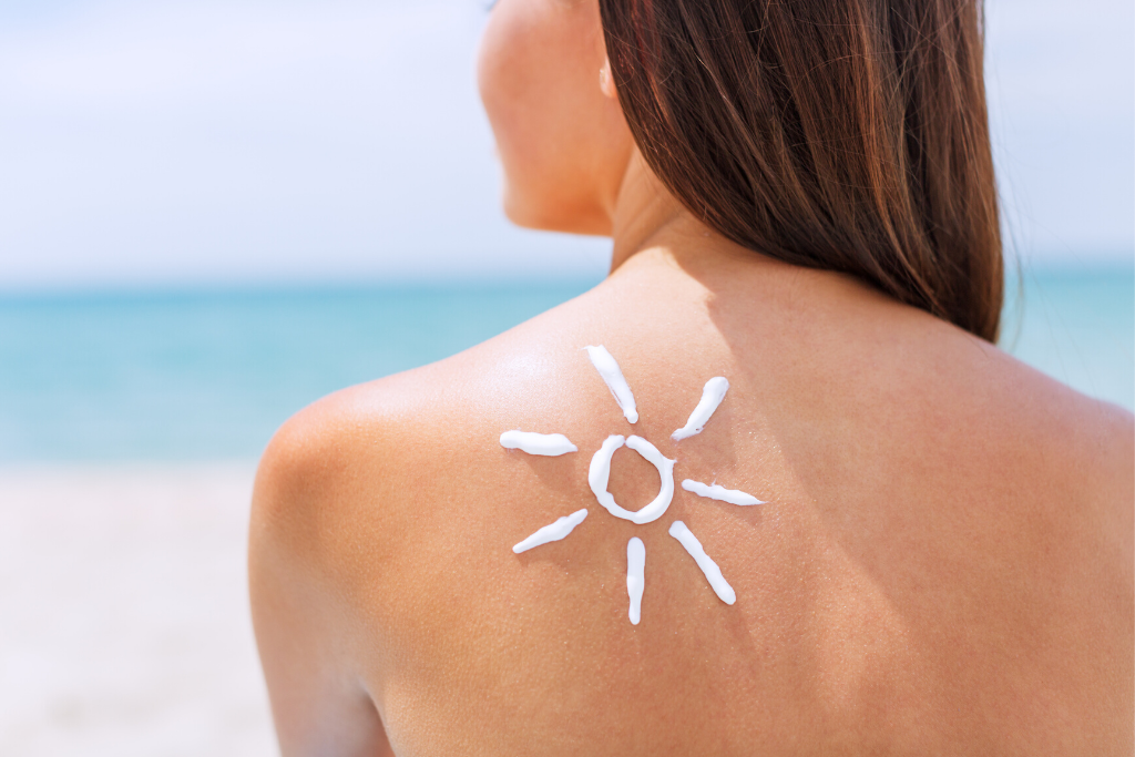 Woman sitting on the beach with a sun drawn on her shoulder with sunscreen. Discover why these 10 expert tips for staying healthy while traveling will make your jetsetting a whole lot more enjoyable! #travelhealth