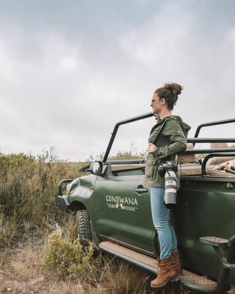 A girl standing on the side of a safari jeep holding a camera. Going on safari is one of the best bucket list experiences anyone can have! #bucketlistexperiences