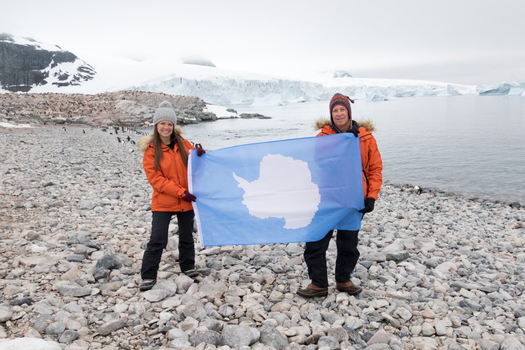 Two people holding up an Antarctica flag. The white continent is one of the most stunning bucket list destinations in the world. #bucketlistdestinations