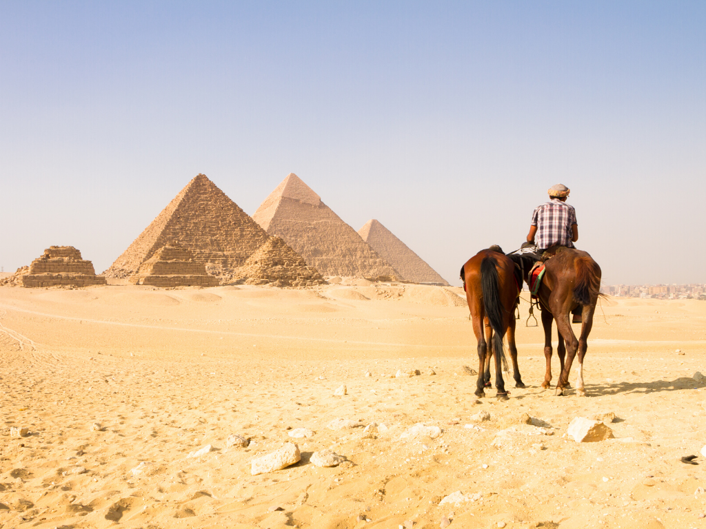 A man riding on a camel near the Great Pyramids. Egypt is one of the most stunning bucket list destinations in the world.