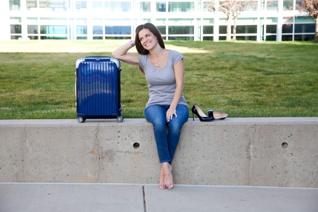 A girl sitting next to a blue Rimowa suitcase, one of the best travel bags on the market!