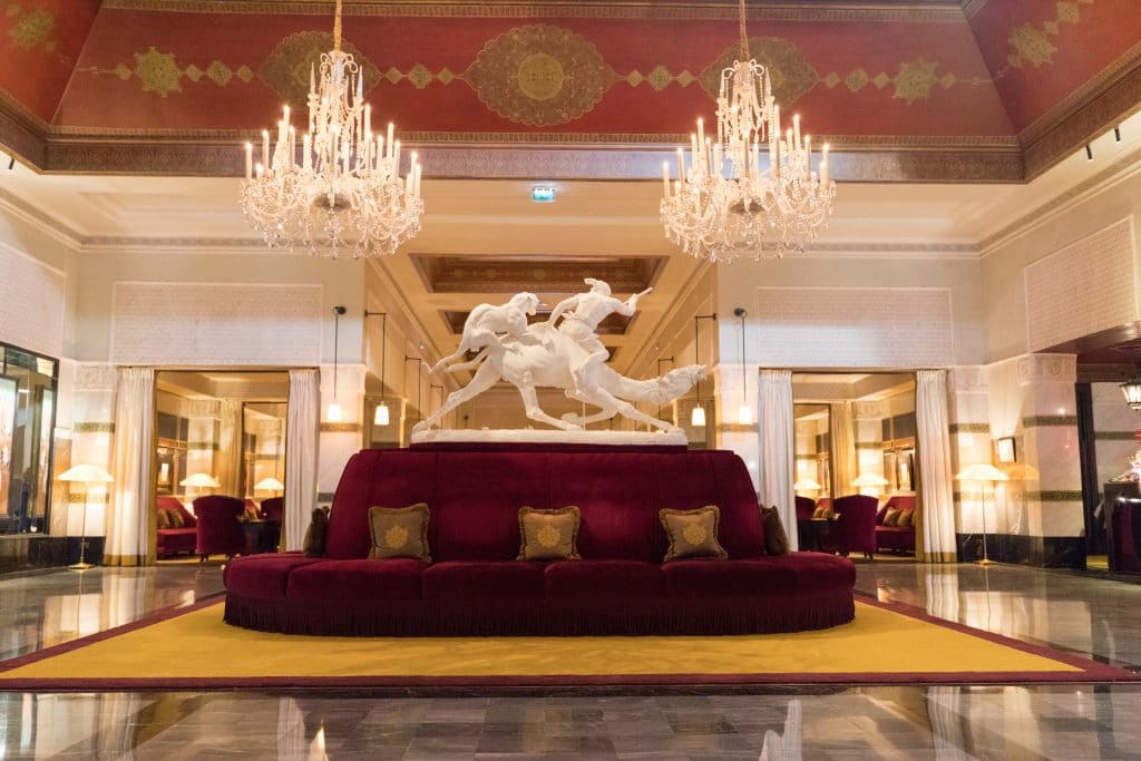 A red couch with a white camel statue and ornate chandeliers at La Mamounia.