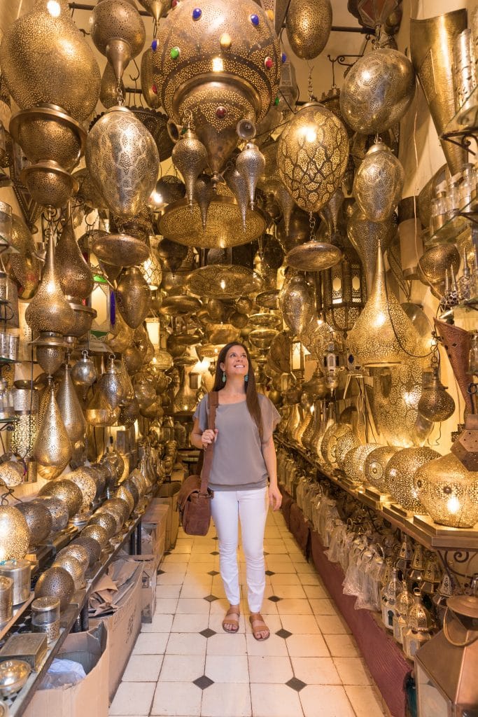 A girl in white pants and a grey top inside a gold lamp shop in the souks. #thingstoknowbeforevisitingmarrakesh