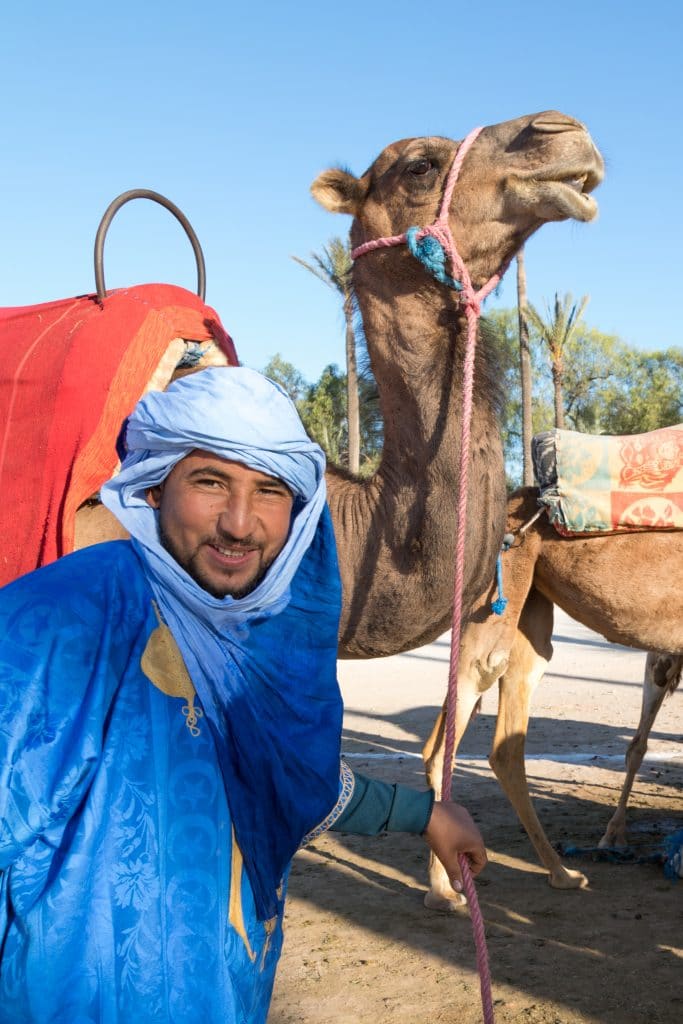 A guide wearing blue standing in front of his camel. #thingstoknowbeforevisitingmarrakesh