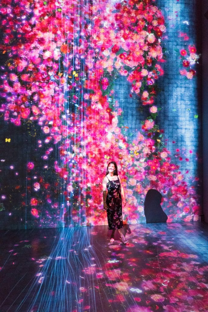 A girl standing against a pink and red flower projection at the ArtScience museum in Singapore. Find out what it's really like to stay at the Marina Bay Sands Singapore. What to expect, what's nearby, and what you shouldn't miss!