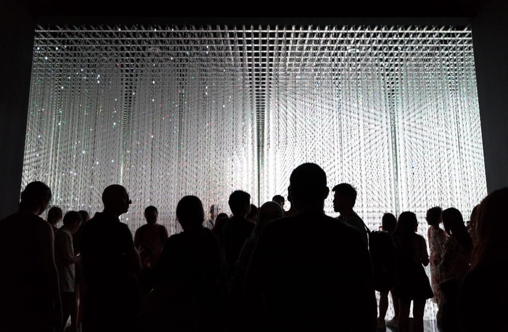 Silhouettes of people against white lights hanging from the ceiling at the ArtScience Museum in Singapore.