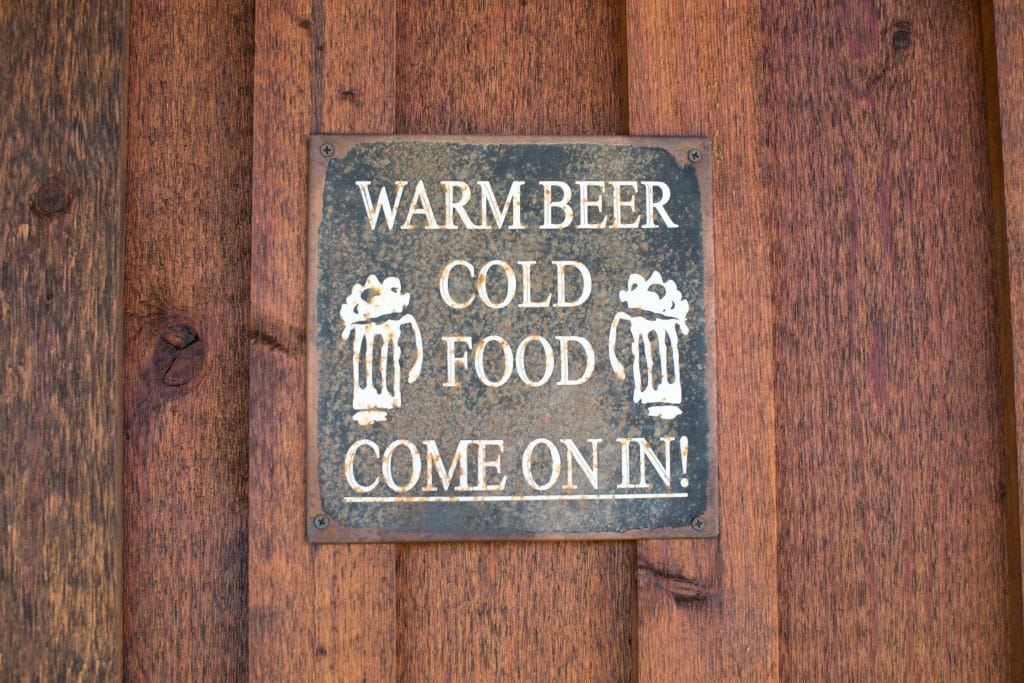A black sign on a cabin that says "warm beer, cold food, come on in!" at Maison Tetonia.