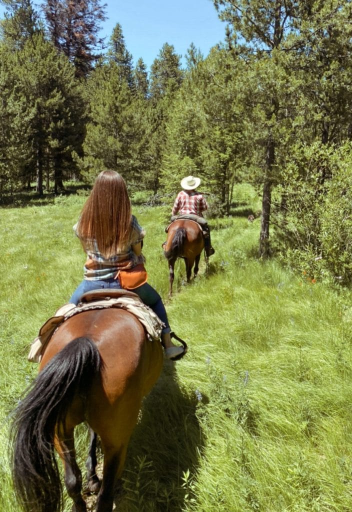 A girl riding a horse behind a cowboy in a red plaid shirt.