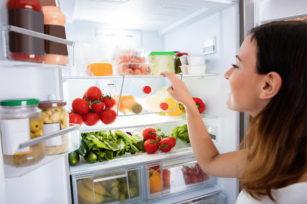 A girl grabbing food from inside a fridge.