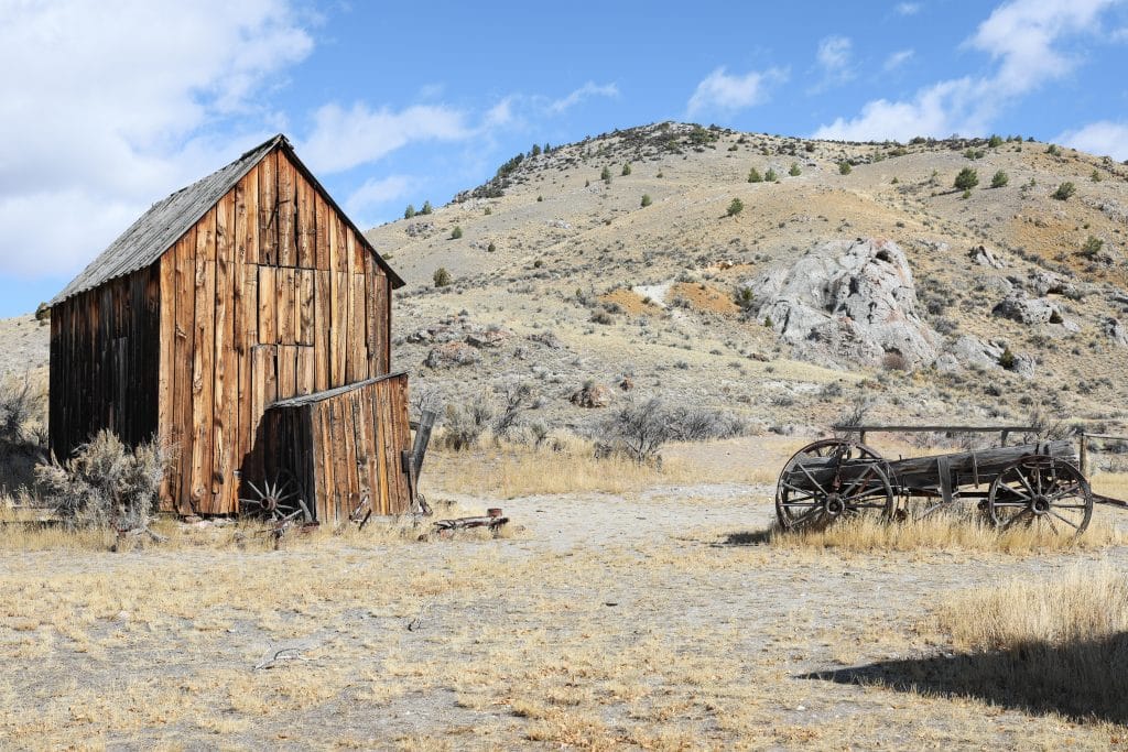 An old wooden barn and a horse-drawn cart. Read on for more history of the ghost town in Bannack Montana.