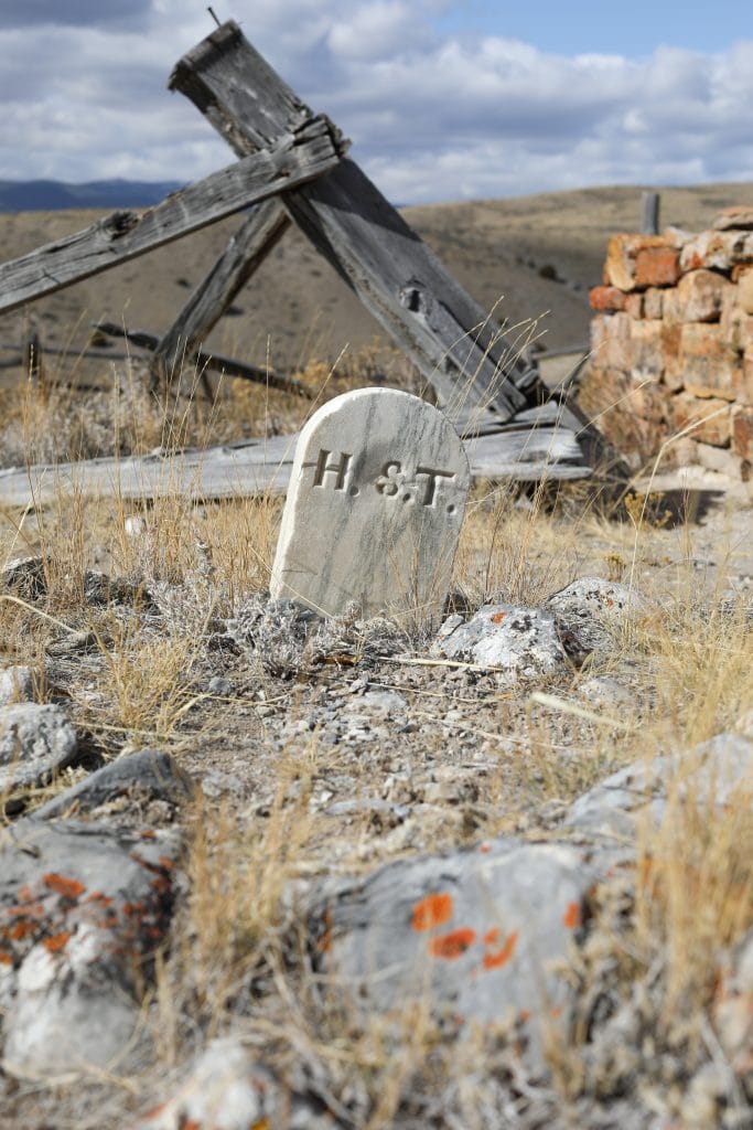 A headstone at a cemetery on a hillside overlooking the ghost town of Bannack Montana.