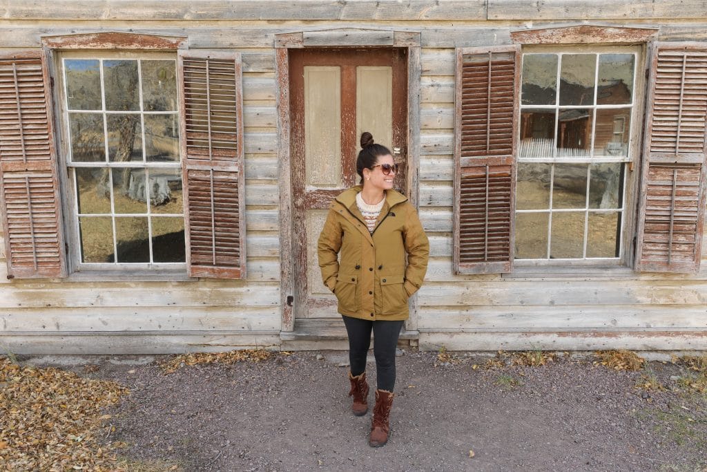 A girl in a yellow coat walking out a front door of an old, abandon cabin in Bannack, Montana.