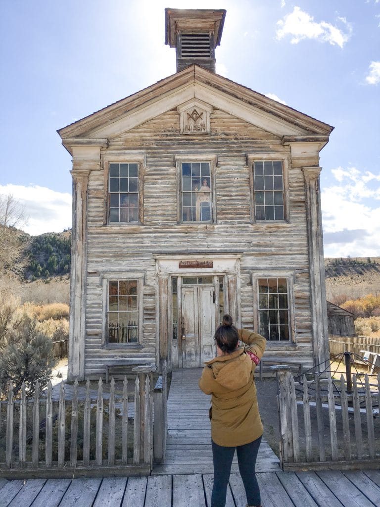 A girl in a yellow coat taking photos of a white schoolhouse.