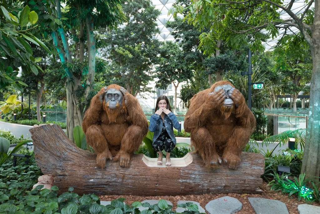 Girl sitting between to orangatan statues on a log at the Changi Airport. #changiairport #canopypark