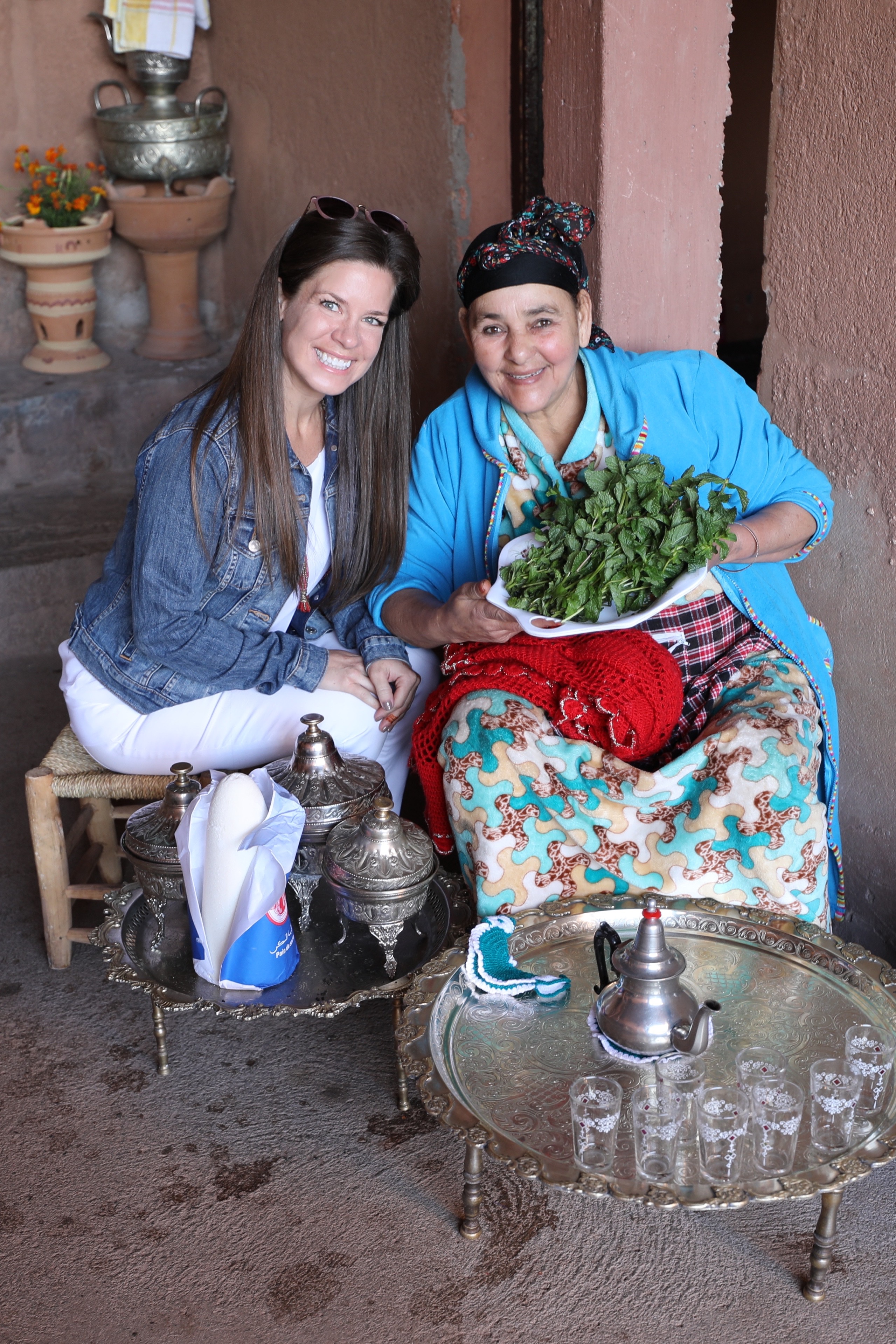 A girl and an older woman holding a bunch of mint leaves in front of a Moroccan tea pot.