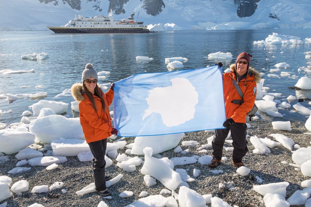 A girl and her father in orange jackets standing on the shores of Antarctica with a cruise ship in the background. Adventures with family is another reason to be thankful for travel.