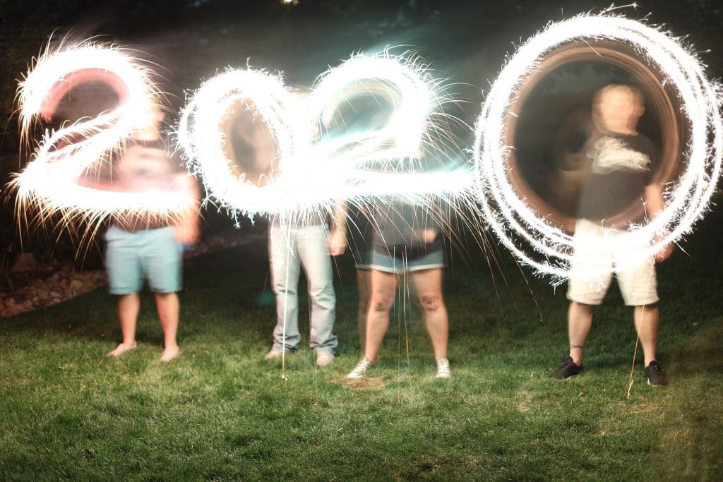 2020 written out in sparklers by four people in a grassy yard.