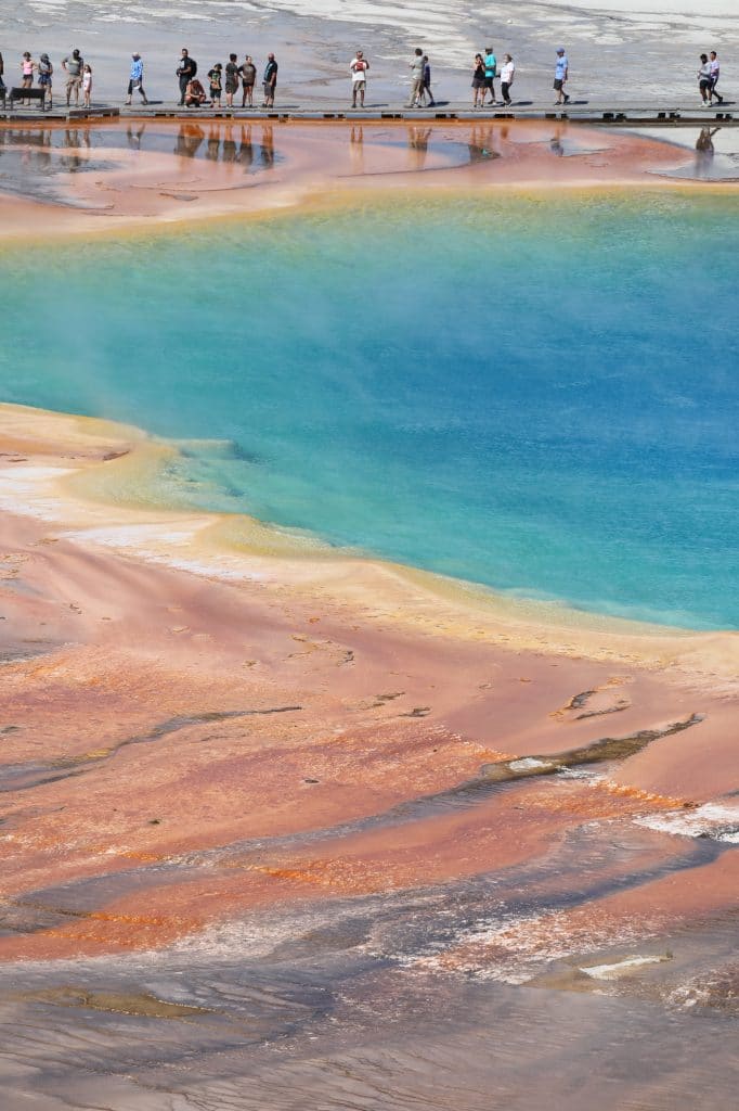 People walking along a boardwalk near a colorful hot spring in Yellowstone.