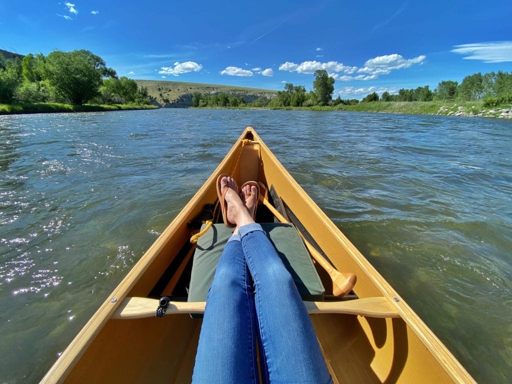 A womans crossed legs in a canoe floating down a river surrounded by trees. One of the most relaxing moments of 2020.