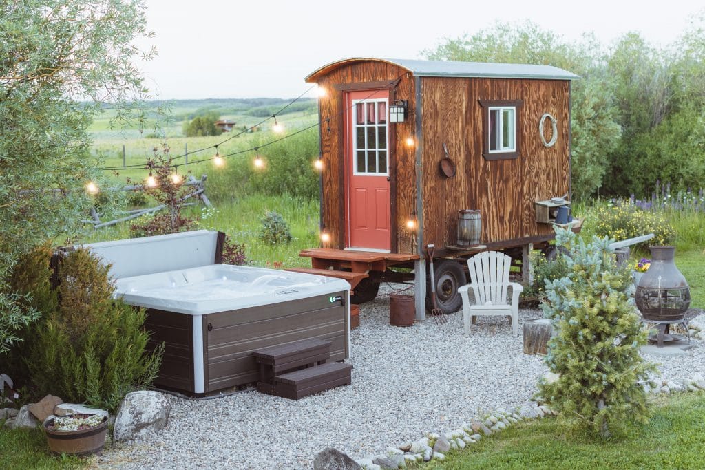 A hot tub with string lights next to an old conestoga wagon surrounded by a field.
