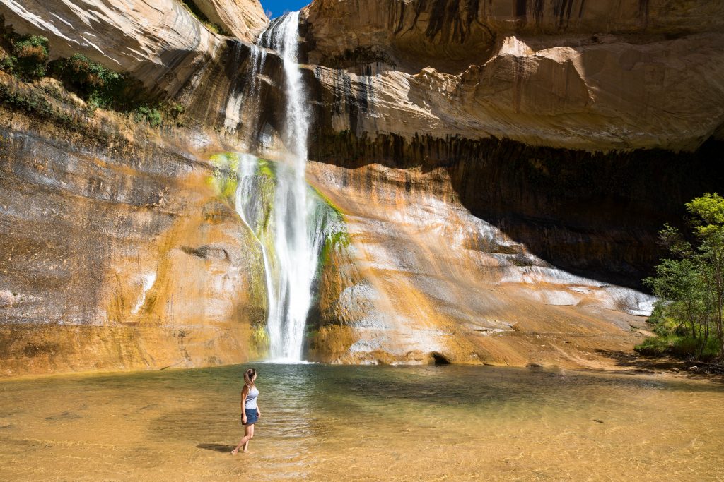 A girl standing in water next to a large mountain waterfall. A scenic pandemic appropriate adventure!
