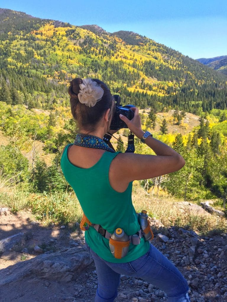 The back of a girl taking a photo in the mountains of the changing aspen colors in Fall.