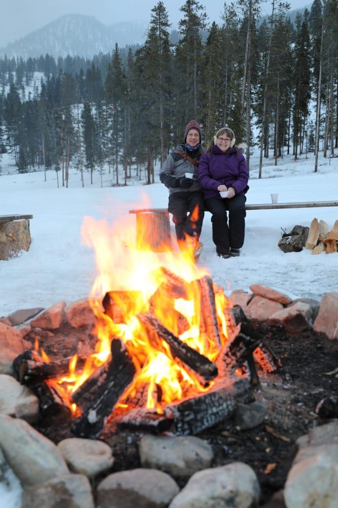 Two people sitting near a fire surrounded by snow. #320guestranch