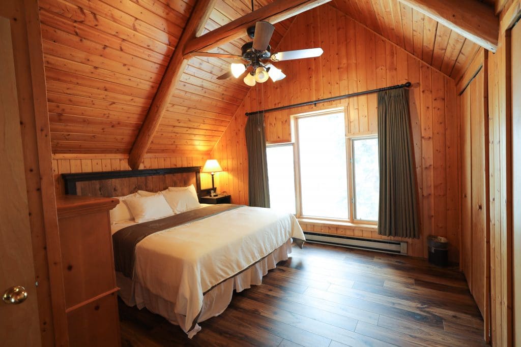 A log cabin bedroom with windows and a ceiling fan at the 320 Guest Ranch. #320guestranch