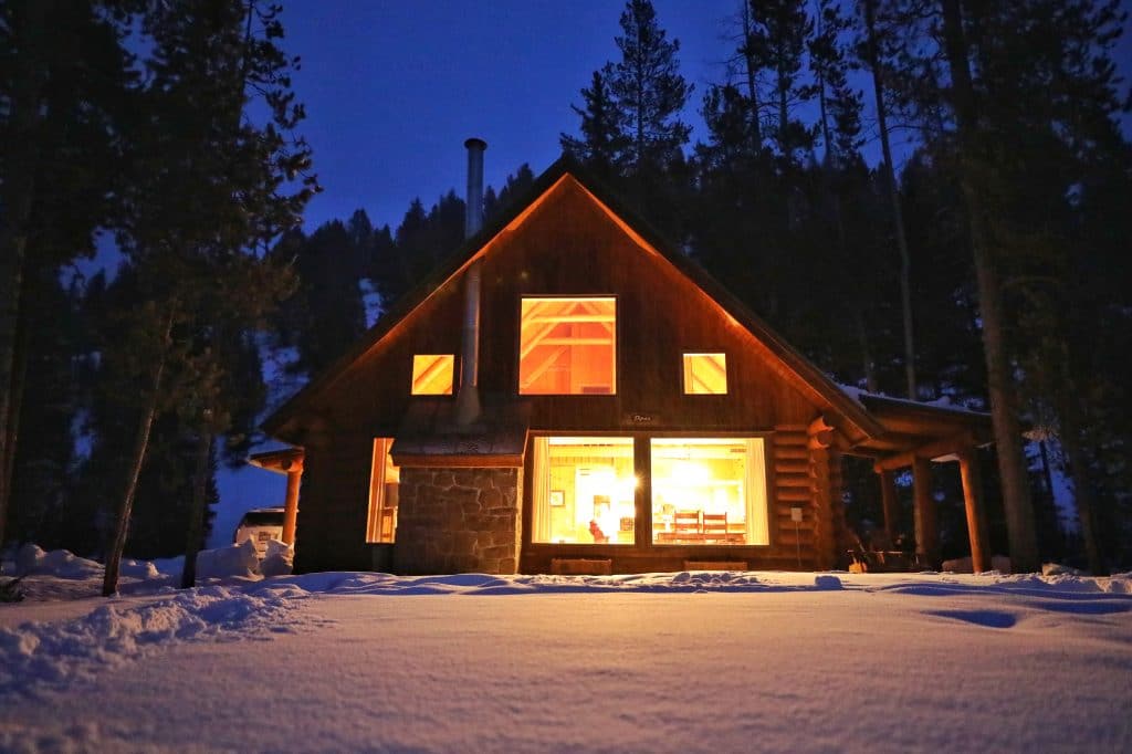 A log cabin at night surrounded by snow at the 320 Guest Ranch. #320guestranch