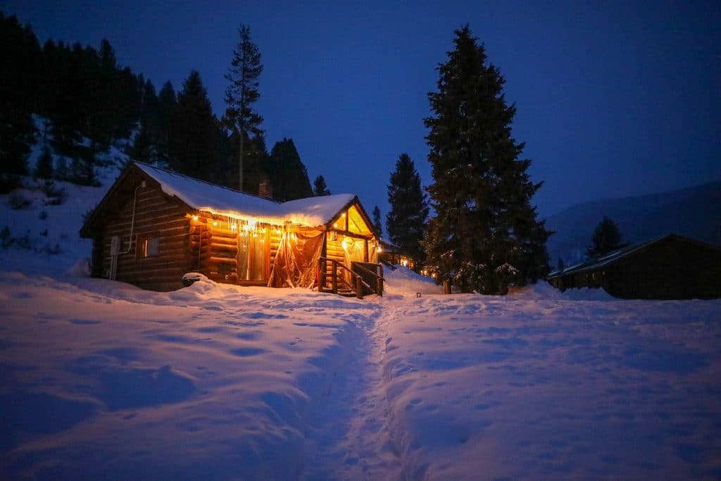 A cabin lit up at night with icycles hanging off the roof and stars in the background. #320guestranch