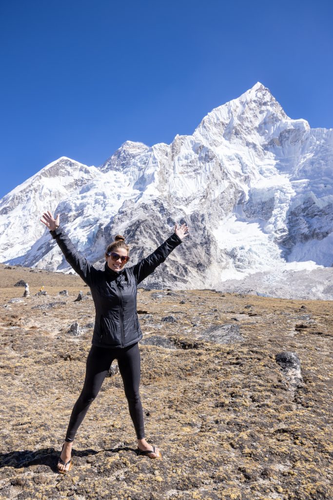 A young woman standing with her arms out in front of Mount Everest.
