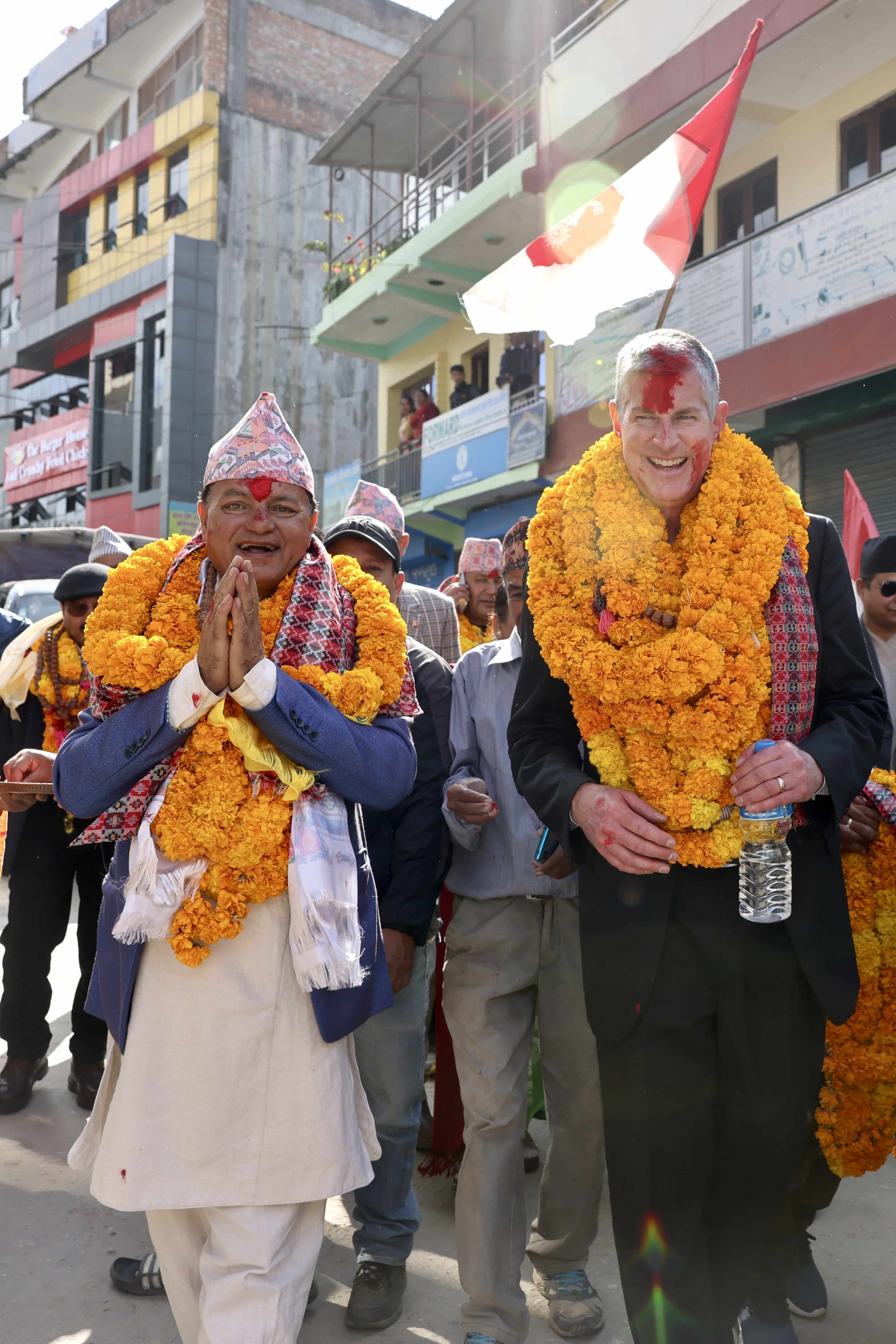 Two men walking with marigold lays in a parade.