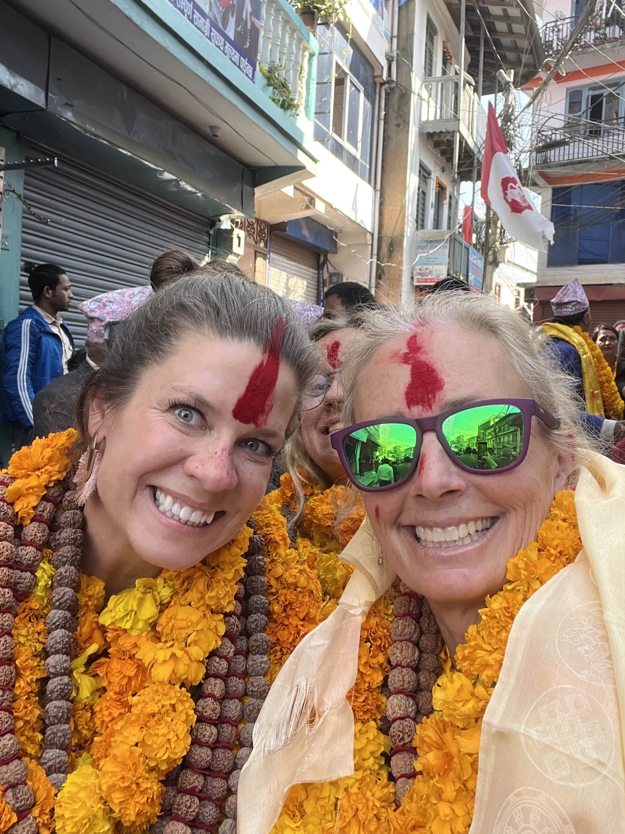 Two women with flower lays and red forehead blessings.