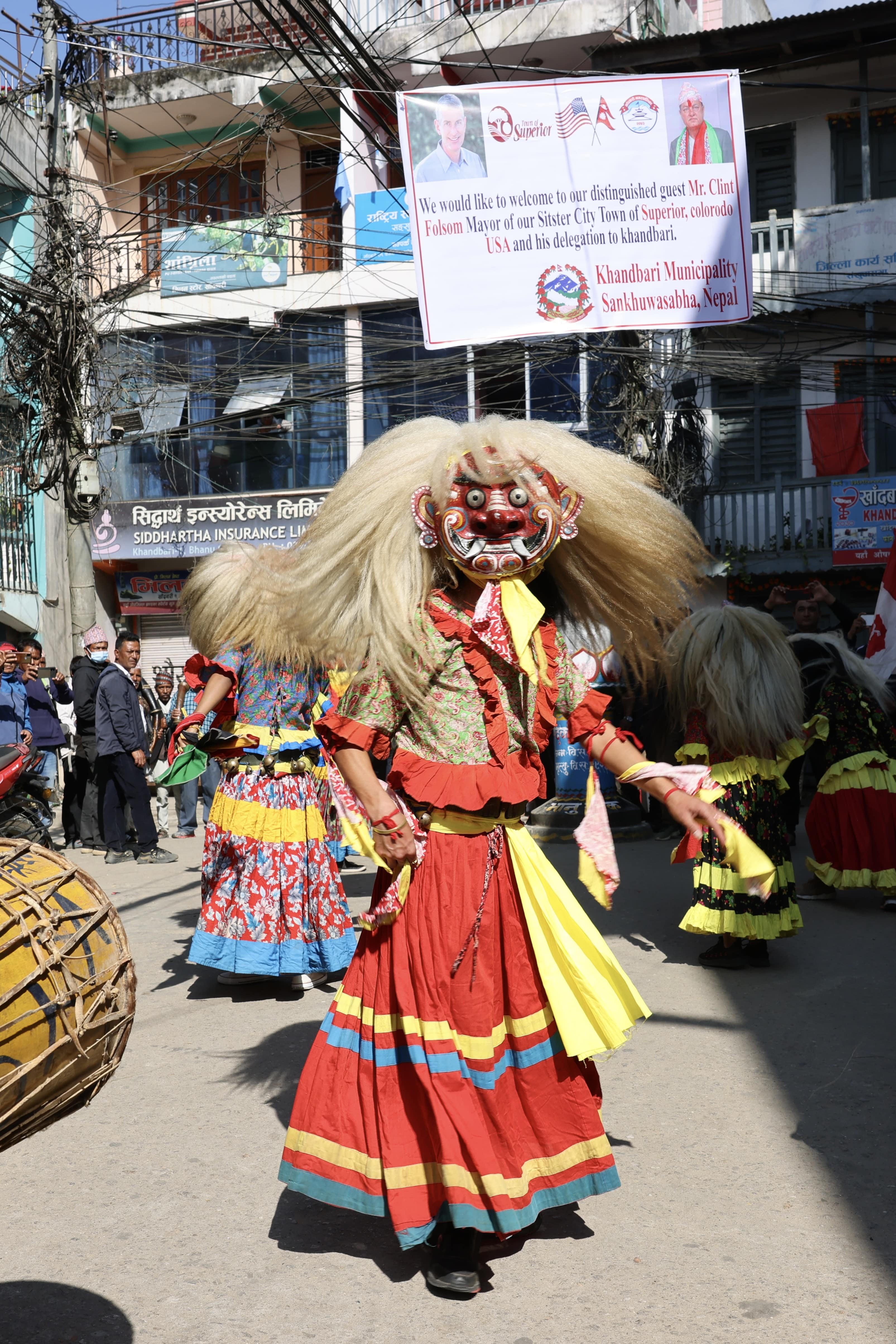 A nepali dancer in a colorful costume and mask with hair.