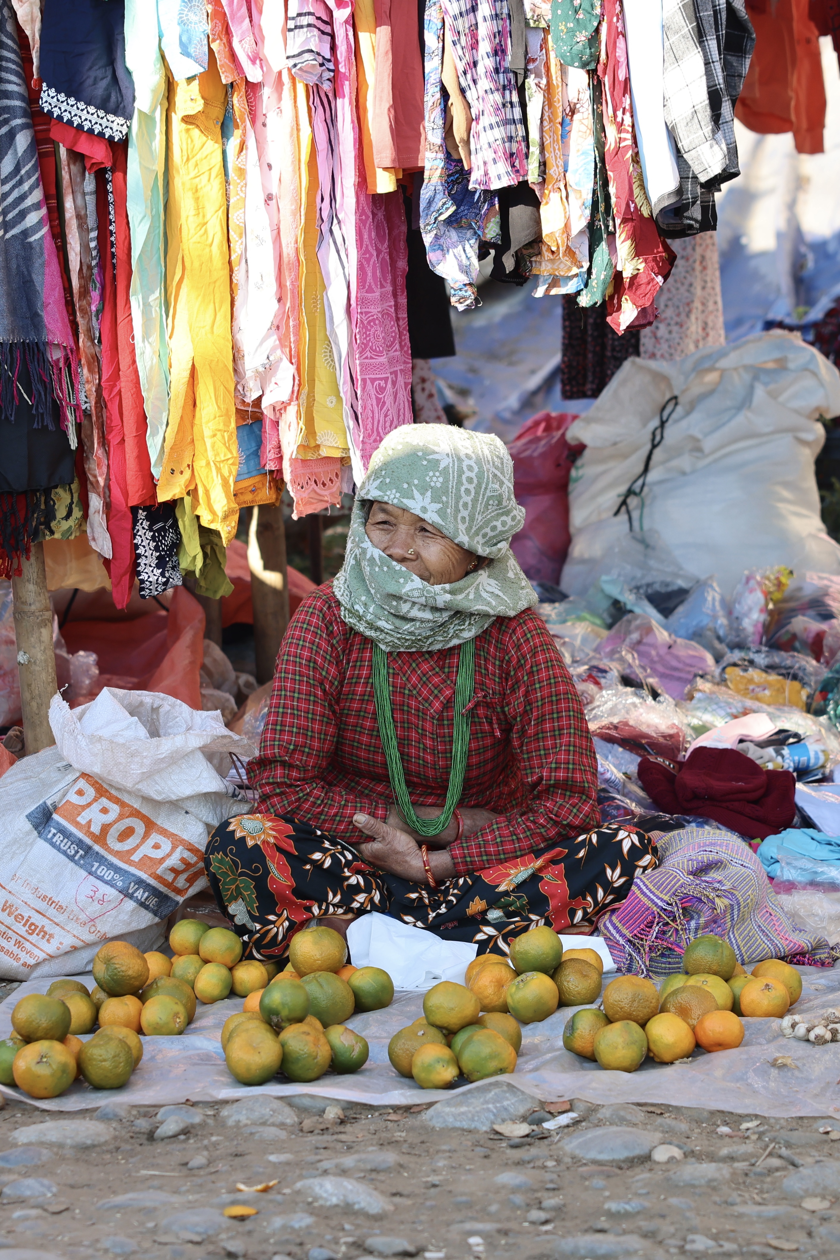 A nepali woman sitting on a tarp surrounded by oranges.
