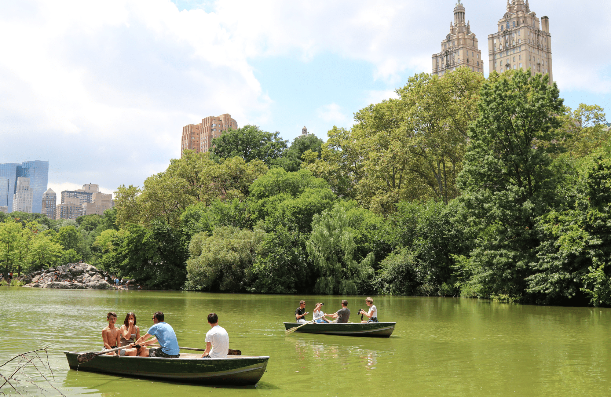 Boats on a lake in Central Park surrounded by trees.