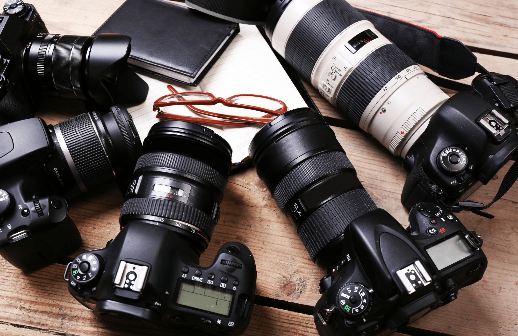 Different cameras sitting next to each other and a pair of glasses.