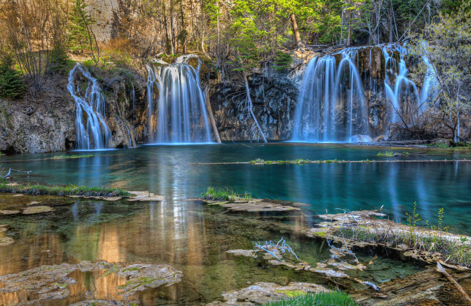 Waterfalls cascading into a lake surrounded by lush green trees.