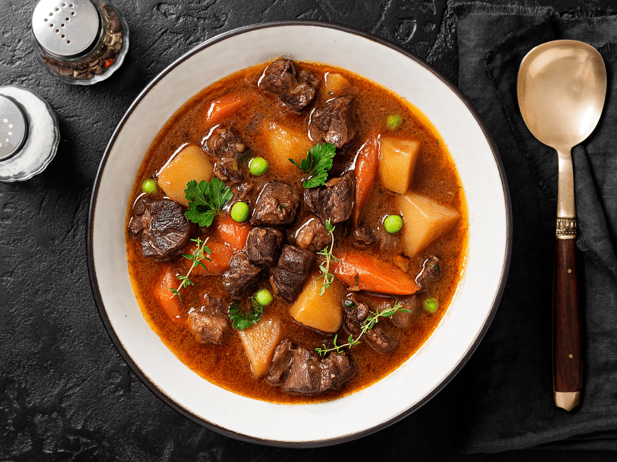 A beef and pumpkin stew next to a spoon with salt and pepper.