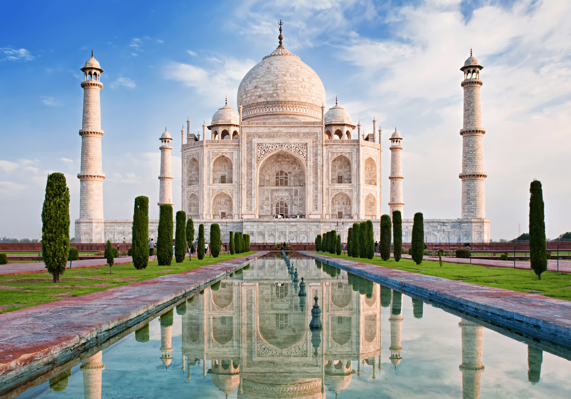 The white facade of the Taj Mahal with the waters of a canal in front of it.