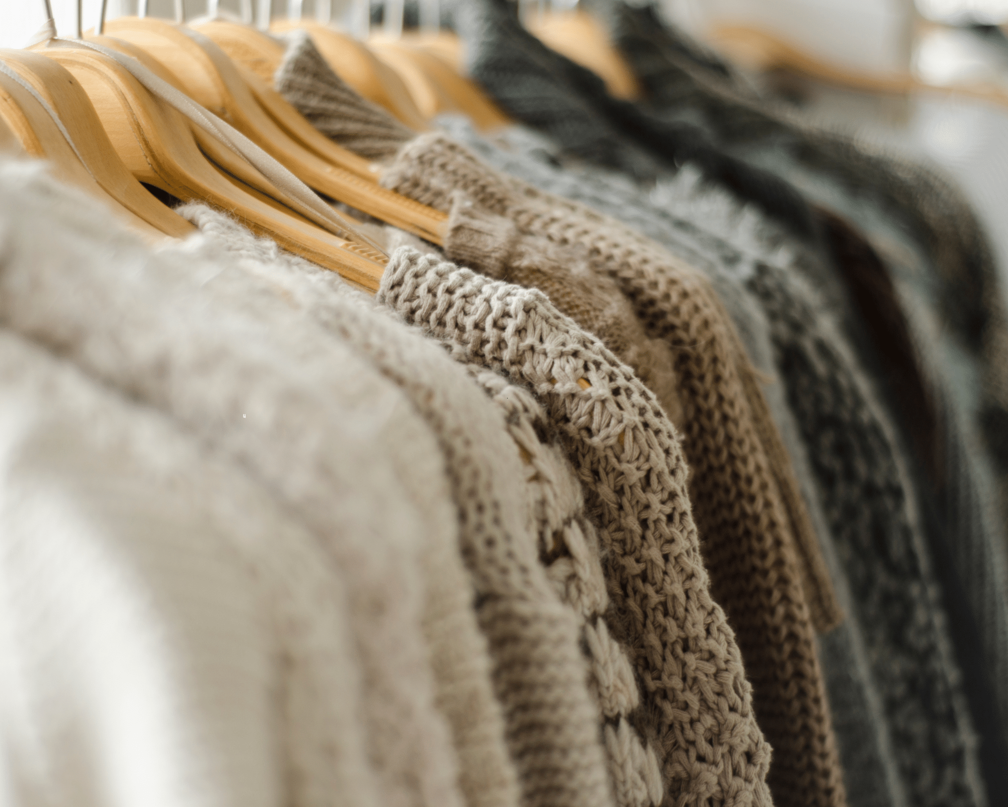 Wool sweaters hung on wooden hangers.