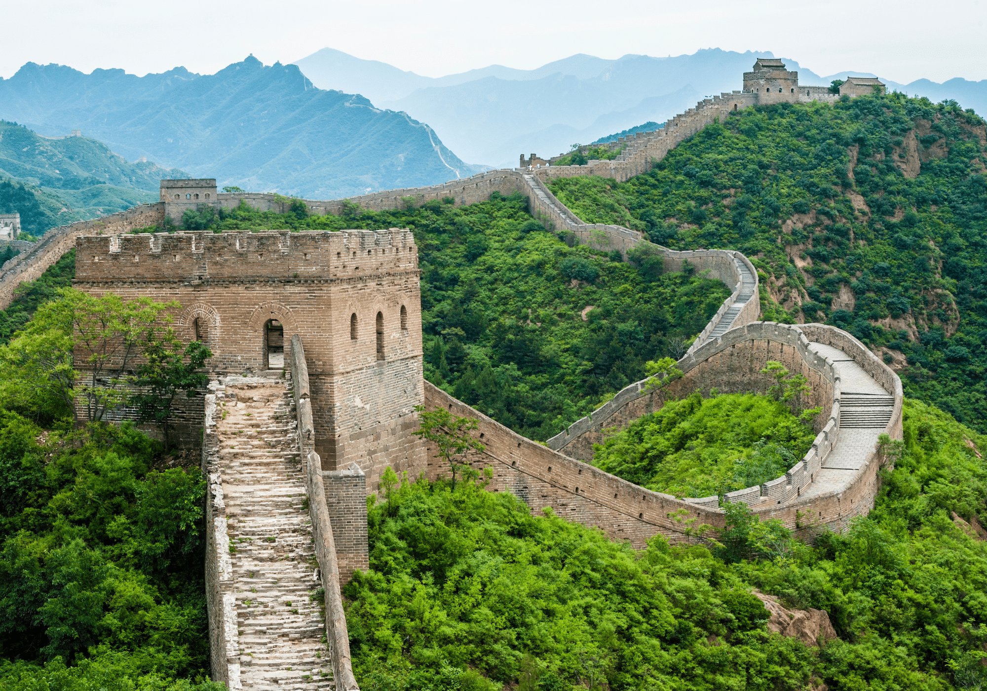 The Great Wall of China spanning miles through a forested mountainside.