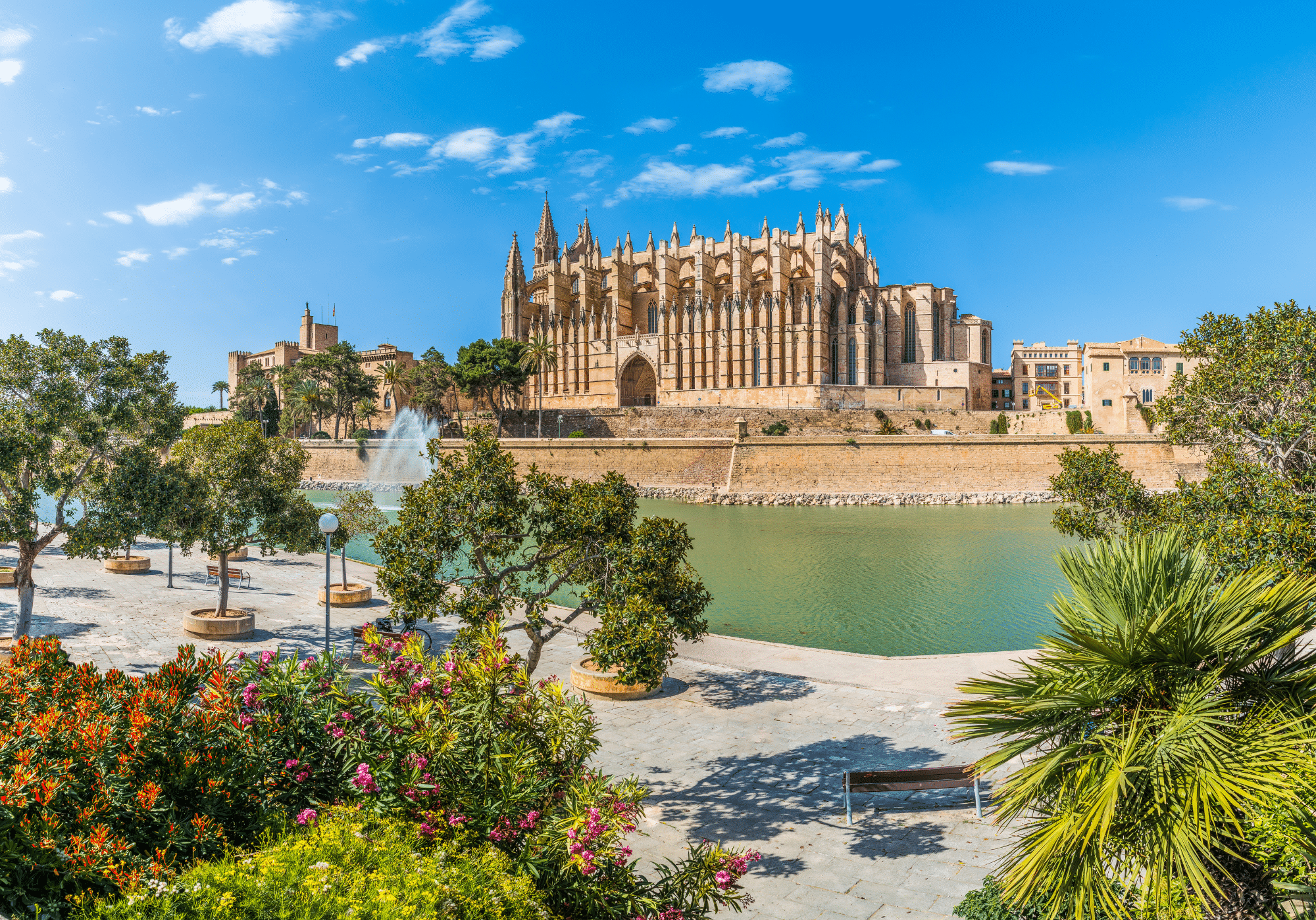 A tan Spanish building in front of water and a paved sidewalk.