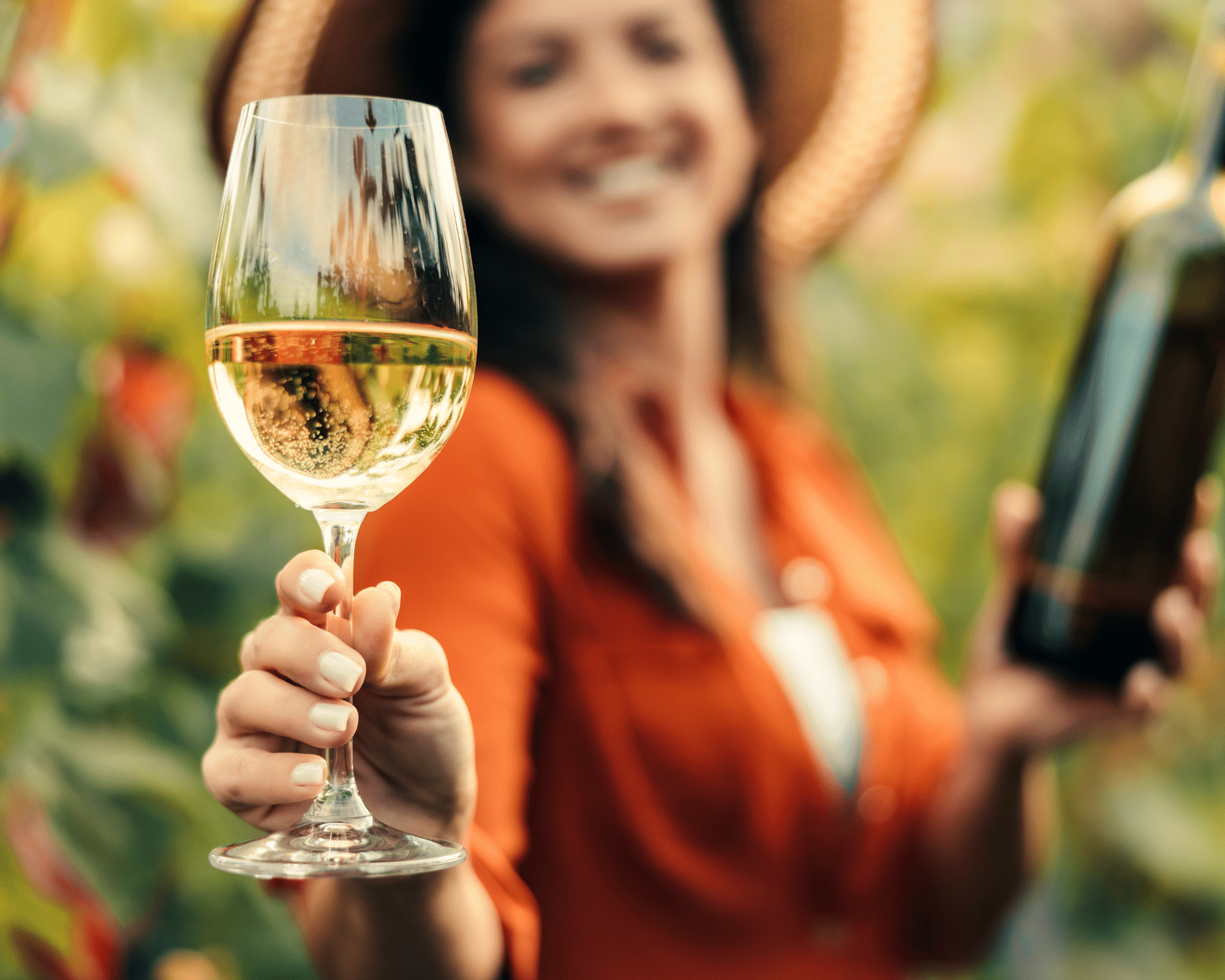 A woman in a hat holding out glass of white wine.