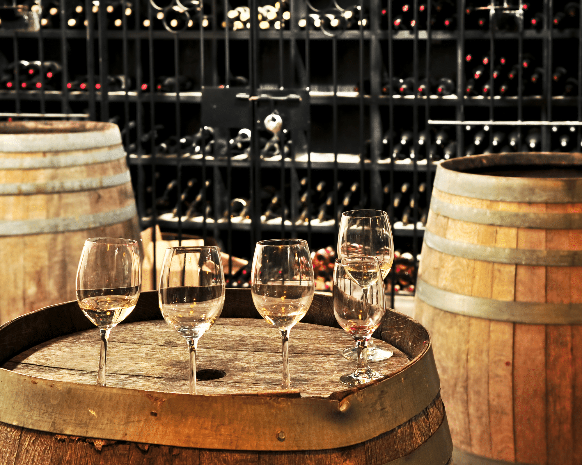 Wine glasses on top of a wooden barrel with wine bottles in the background.